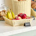 A rectangular woven plastic rattan basket filled with fruit and bread on a counter.
