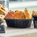 An Acopa black woven plastic rattan bread basket filled with pastries on a table.