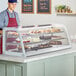 An Avantco white curved refrigerated countertop bakery display case filled with pastries and cupcakes.