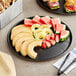 A Solut black catering tray with a variety of fruit and sandwiches on a table.
