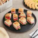 A Solut black corrugated catering tray with sandwiches, fruit, and tongs on it.
