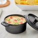 A black Elite Global Solutions faux cast iron melamine pot with a lid filled with sauce.