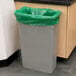 A grey trash can with a green low density liner.