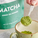 A hand holding a spoonful of Tenzo matcha green tea powder.