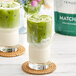 A close-up of a matcha green tea latte with green liquid and white foam.