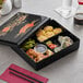 A black rectangular Emperor's Select bento box with food inside.