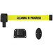 A yellow Banner Stakes retractable belt with black text reading "Cleaning in Progress" attached to a black oval wall mount.