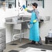 A person in a blue apron and gloves using a Steelton 3-compartment sink in a professional kitchen.