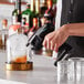 A man using a Flavour Blaster Black Pro 2 Cocktail Gun to smoke a drink in a glass on a counter in a cocktail bar.