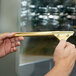 A hand holding a Unger brass channel for window cleaning with a gold metal clip.