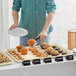 A man using a Baker's Mark wire rim aluminum sheet pan to serve pastries on a table in a bakery.