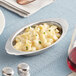 An oval stainless steel au gratin dish filled with pasta and cheese sauce.