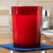 A red Cambro Del Mar plastic tumbler with red liquid and a candle on a table.