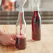 A hand pouring red liquid into a 375 mL Burgundy wine bottle.