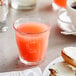 A glass of Ocean Spray Ruby Red grapefruit juice on a table next to a plate of food.
