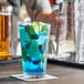 A stackable Acopa Select Cooler/Mixing glass filled with a blue drink with limes and ice.