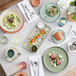 A table with Acopa Pangea fog white matte porcelain bowls and plates of food.