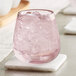 A Mauve Acopa stemless wine glass filled with pink liquid and ice on a coaster on a table.
