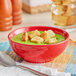 A close-up of a red Acopa Capri stoneware bowl of green soup with croutons.