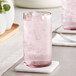An Acopa mauve beverage glass filled with pink liquid and ice on a white coaster.