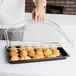 A person using a Cambro clear dome display cover to serve croissants on a tray.
