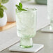 An Acopa Pangea green goblet with ice, mint, and lime on a table.