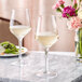 Two Acopa Silhouette wine glasses on a marble table with white wine and flowers.