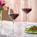 Two Acopa Silhouette wine glasses filled with red wine on a marble table with food.