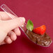 A hand holding a WNA Comet clear plastic Asian soup spoon filled with chocolate pudding with a strawberry on top.