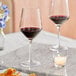 A pair of Acopa Silhouette wine glasses on a marble table with a glass of red wine.