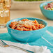 A Caribbean turquoise Acopa Capri bistro bowl filled with pasta and salad with a spoon on a cloth.
