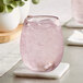 A close up of a Mauve Acopa Pangea stemless wine glass with ice and pink liquid on a white coaster.