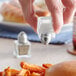 A hand holding a Choice mini salt shaker over a sandwich.
