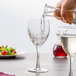 A hand pouring wine into a tall Arcoroc wine glass on a table with food.