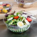 A salad with leafy greens, broccoli, and a hard boiled egg in a Dart clear plastic bowl with a clear dome lid.