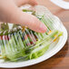 A hand using a Dart clear plastic dome lid to cover a plastic container of salad.