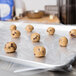 A tray of cookie dough balls on a sheet pan lined with a white and brown 18" x 26" Full Size Bun Pan liner.