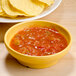A GET Tropical Yellow Salsa Dish filled with salsa next to chips on a table.