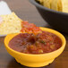 A chip dipping into a yellow bowl of salsa.