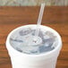 A Dart translucent lid with a straw slot on a white cup of ice with a straw in it.
