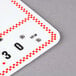 A red and white checkered deli tag wheel with white write-on labels with red and black numbers.