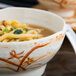 A bowl of noodles with broth in a Thunder Group Gold Orchid melamine bowl.