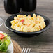 A black Tuxton Concentrix China bowl filled with macaroni and cheese on a table with salad.