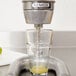 A Nemco manual citrus juicer on a counter with a glass of juice being poured.