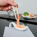 A person holding chopsticks over a spoon with a shrimp on it.