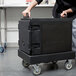 A person pushing a black Cambro Camdolly with a black rectangular box on it.