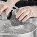 A hand in a glove using a Choice stainless steel scrubber to clean a pan.