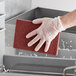 A gloved hand uses a Lavex maroon scouring pad to clean a kitchen counter.