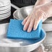 A hand in a plastic glove cleaning a pan with a Lavex blue sponge.