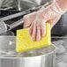 A person in gloves cleaning a pan with a yellow Lavex sponge.